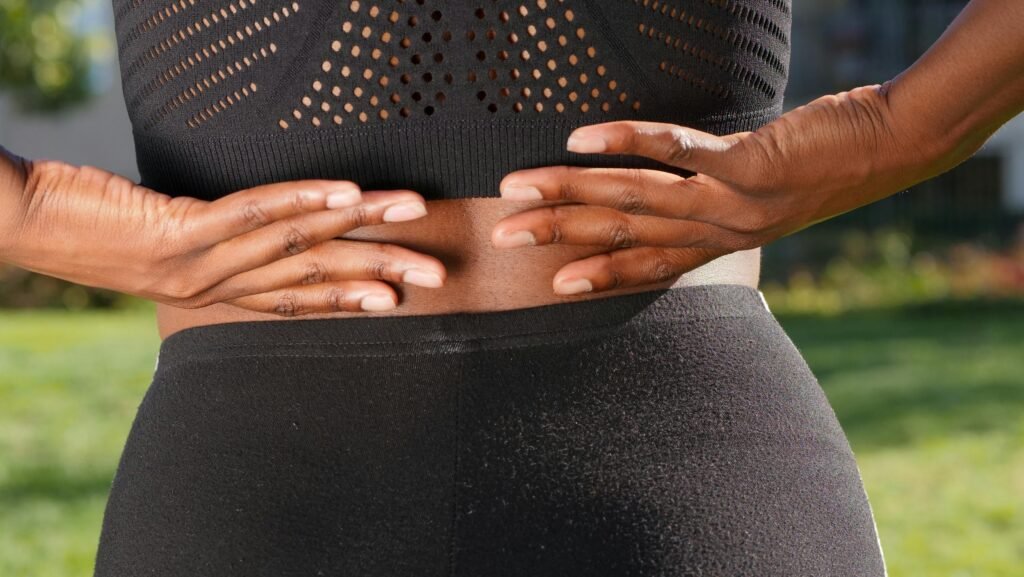 Close-up of a woman's hands gripping her painful back while outdoors.