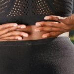 Close-up of a woman's hands gripping her painful back while outdoors.
